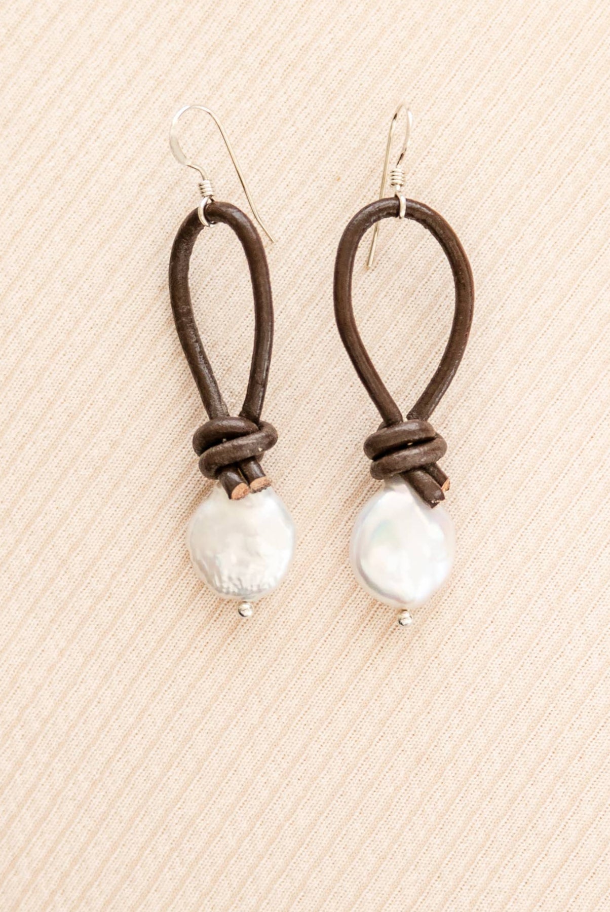 Pair of earrings with brown leather loops and white beads on a beige textured background
