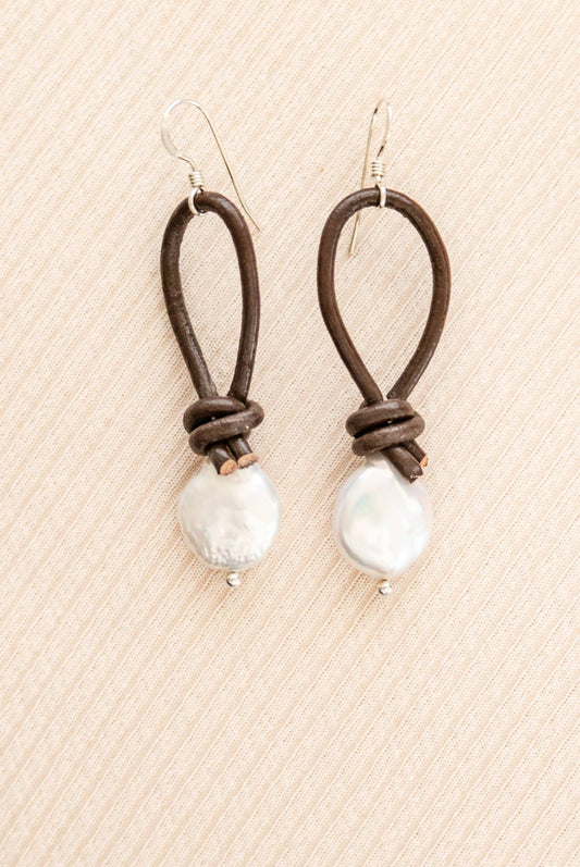 Pair of earrings with brown leather loops and white beads on a beige textured background